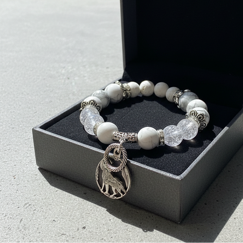 Bracelet with white beads and a lion charm on a black jewelry box.
