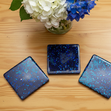 Load image into Gallery viewer, Three square blue glittery coasters on a wooden surface