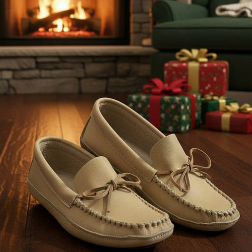 Pair of beige loafers on a wooden floor with a fireplace and green sofa in the background.