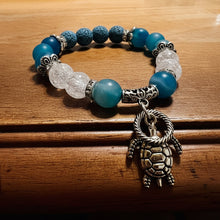 Load image into Gallery viewer, Bracelet with blue and white beads and a turtle charm on a wooden surface