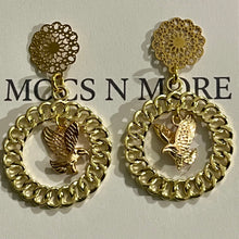 Load image into Gallery viewer, A pair of gold-tone dangle earrings displayed on a white card. Each earring has a circular floral filigree stud, a large textured circular drop, and a small eagle motif in the center.