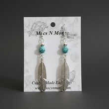 Load image into Gallery viewer, Feather-shaped earrings with turquoise beads on a Mecs N More branded card.