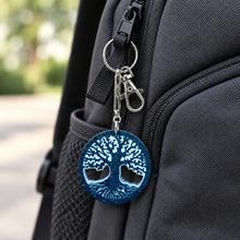 Load image into Gallery viewer, A handmade keychain featuring a circular blue and white tree of life pendant, attached to a silver clasp and a brown kraft paper display card that reads 'Handmade with love'.