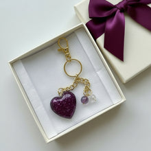 Load image into Gallery viewer, Purple heart-shaped keychain with gold chain in a gift box with a purple ribbon.