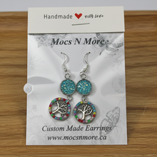 Load image into Gallery viewer, Pair of custom-made earrings on a Mocs N More branded card on a wooden surface.