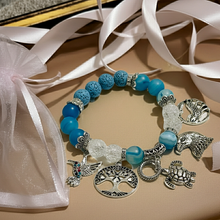 Load image into Gallery viewer, Bracelet with blue beads and silver charms on a beige surface with white ribbon