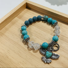 Load image into Gallery viewer, Bracelet with blue beads and silver charms on a beige surface