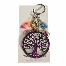 Load image into Gallery viewer, A purple glitter tree of life keychain with a silver metal clasp and key ring, attached to a white display card, set against a green patterned fabric background.