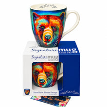 Load image into Gallery viewer, A ceramic mug featuring a colorful, stylized bear face illustration, displayed next to its white and blue retail packaging box on a plain white background.