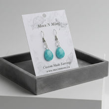 Load image into Gallery viewer, Turquoise glitter teardrop earrings on a Mocs N More branded card with Christmas decorations in the background.