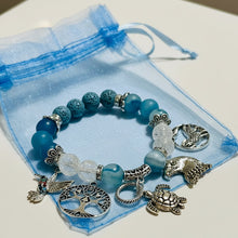 Load image into Gallery viewer, Blue beaded bracelet with silver charms on a blue drawstring bag