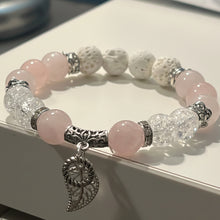 Load image into Gallery viewer, A beaded stretch bracelet featuring light pink rose quartz beads, textured white lava stones, clear faceted crystal beads, and silver-toned metal spacers with a dangling silver angel wing charm, resting on a white surface.