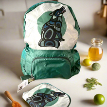 Load image into Gallery viewer, Green backpack with a white front panel featuring a black and blue design on a table.