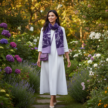 Load image into Gallery viewer, A woman stands in a lush garden wearing a long white dress, a purple patterned scarf, and carrying a small purple handbag.