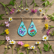 Load image into Gallery viewer, Teal teardrop Indigenous art earrings flat lay on wood with wildflowers