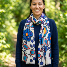 Load image into Gallery viewer, A woman smiling outdoors in a forest setting, wearing a navy blue sweater and a white scarf with a colorful floral pattern in blue, red, and orange.