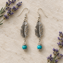 Load image into Gallery viewer, Silver feather earrings on a light counter with lavender