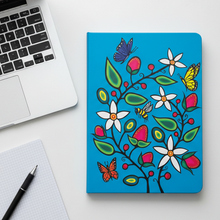 Load image into Gallery viewer, Colorful notebook with floral and butterfly design on a white surface with a laptop and pen.